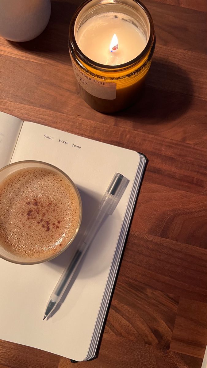 An open notebook, pen and cappuccino by candlelight